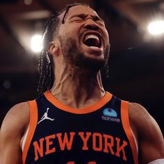 a man with dreadlocks and an orange jersey is laughing while standing in the middle of a basketball court