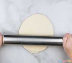 two hands are rolling out the dough on a marble counter top with a pizza roller