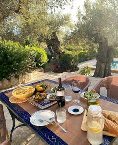 a table with food and wine on it in front of an outdoor swimming pool area