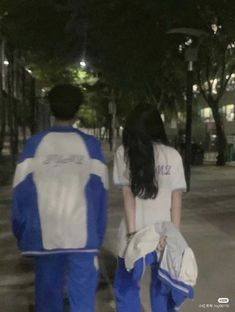 two people walking down the street at night with one person wearing blue and white clothing