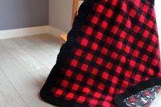 a red and black plaid blanket sitting on top of a wooden floor next to a chair