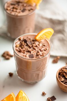 two glasses filled with chocolate pudding and orange slices on a white surface next to other desserts