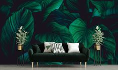 a living room with a black couch and green leaves on the wall behind it,