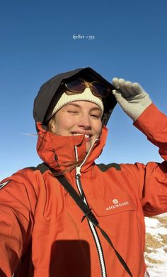 a woman in an orange jacket is smiling and holding her hands up to her head