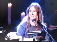 a man with long hair sitting in front of a microphone