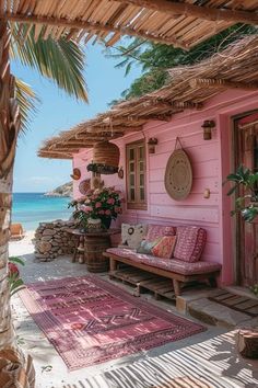 a pink house on the beach with an area rug and potted plants next to it