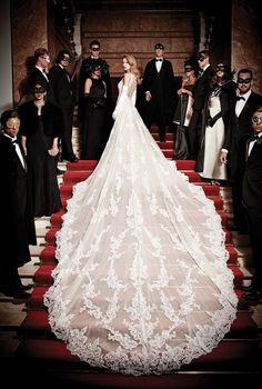 a woman in a white wedding dress standing on stairs with other people behind her and wearing black tuxedos