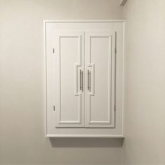 a white cabinet with two doors on the wall in a room that appears to be empty