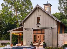 an outdoor swimming pool in front of a barn style house with a hot tub and covered patio