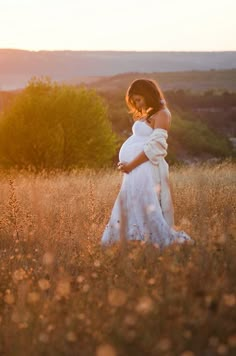 a pregnant woman standing in a field at sunset