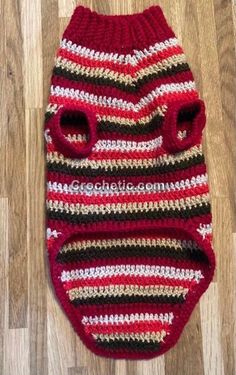 a crocheted red and black striped dog sweater with holes in the middle on a wooden floor