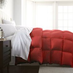 a bed with a red comforter and white sheets on it's headboard