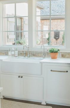 a white kitchen sink sitting next to a window with potted plants on the counter