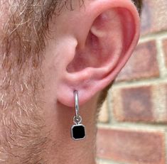 a man wearing an earring with a square shaped black stone hanging from it's side