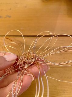 a person is holding some kind of wire on a wooden table and it looks like they are making something out of yarn