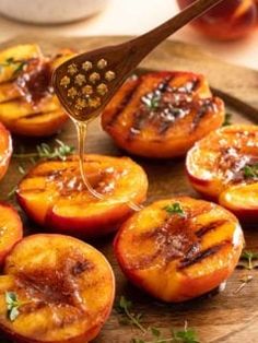 grilled peaches on a wooden platter being drizzled with honey