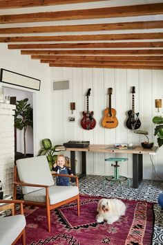 a small child sitting in a chair next to a table with guitars on the wall