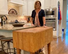 a woman standing at the end of a kitchen island with a cutting board on it