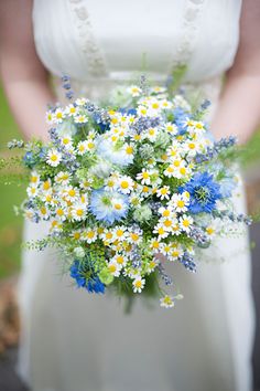 a woman holding a bouquet of wildflowers and daisies on her wedding day