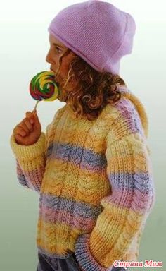 a young child holding a lollipop while wearing a knitted sweater and hat