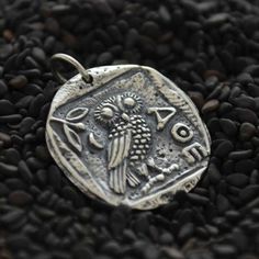 an ancient coin is sitting on some black rocks and gravel, with the image of a bird