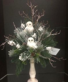 a white vase filled with lots of snow covered plants and birds sitting on top of it