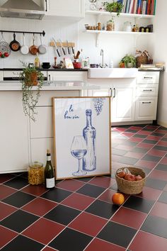 a kitchen with red and black tile flooring, white cupboards and an open wine bottle on the counter