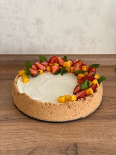 a cake decorated with strawberries and mangos on top of a wooden table in front of a white wall