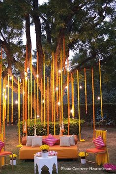 an outdoor seating area is decorated with yellow and pink ribbons, candles, and pillows