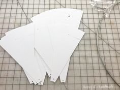 four pieces of white paper laid out on top of a cutting mat with scissors and thread