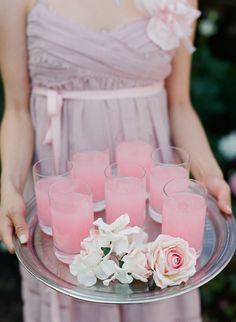 a woman holding a tray with pink candles and white flowers on top of her plate