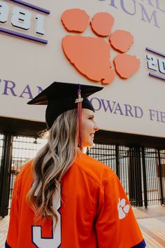 a woman in an orange shirt and black cap is standing outside the clemson football stadium