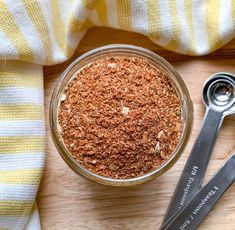 a jar filled with spices next to two spoons on top of a wooden table