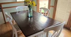 a dining room table with white chairs and a vase filled with yellow flowers on it