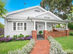 a white house with red brick walkway leading to the front door and side entrance, surrounded by greenery