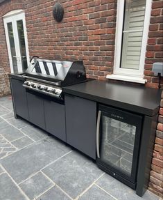 an outdoor bbq and oven on the side of a brick building with white windows