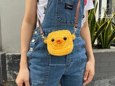 a woman wearing overalls and holding a yellow crocheted chicken bag with eyes