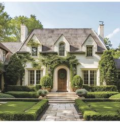 a large white house with lots of hedges and bushes around it's front door