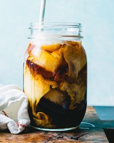 a glass jar filled with liquid sitting on top of a wooden table next to a white towel