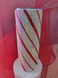 a red and white vase sitting on top of a white stand next to a pink net