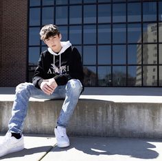 a young man sitting on top of a cement step wearing a black hoodie and jeans