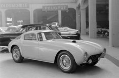 an old photo of a car parked in front of a building with other cars behind it