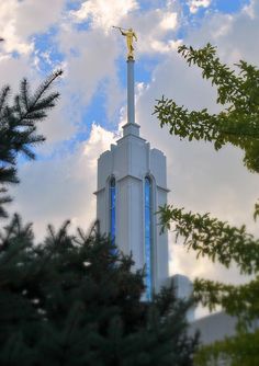 a church steeple with a golden statue on it's side and trees in the foreground