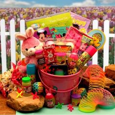 a pink bucket filled with lots of toys on top of a wooden table next to a white picket fence