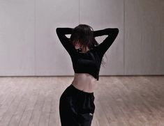 a woman standing on top of a hard wood floor next to a white wall with her hands behind her head