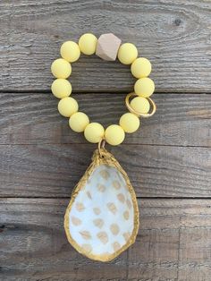 a yellow beaded bracelet with a white shell hanging from it's side on a wooden surface