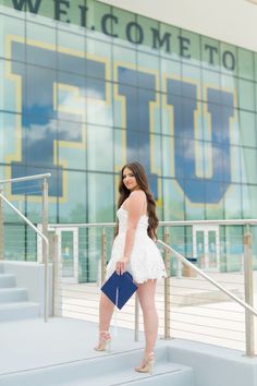 a woman in white dress standing on steps with her purse and looking at the camera