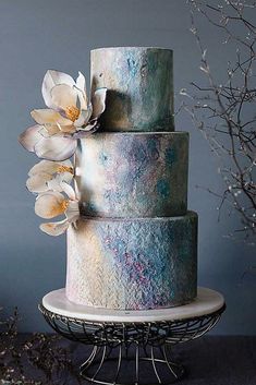 there is a three layer cake with flowers on the top and bottom, sitting on a stand