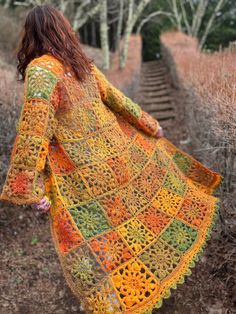 a woman walking down a path wearing a colorful crocheted blanket over her shoulders