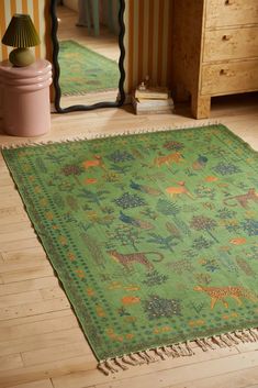 a green rug with animals on it in a room next to a mirror and dresser